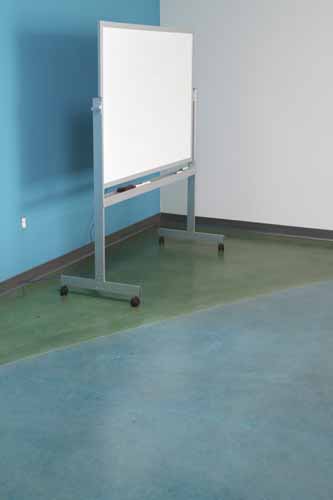 A whiteboard sits on green stained concrete floor in a bright room.